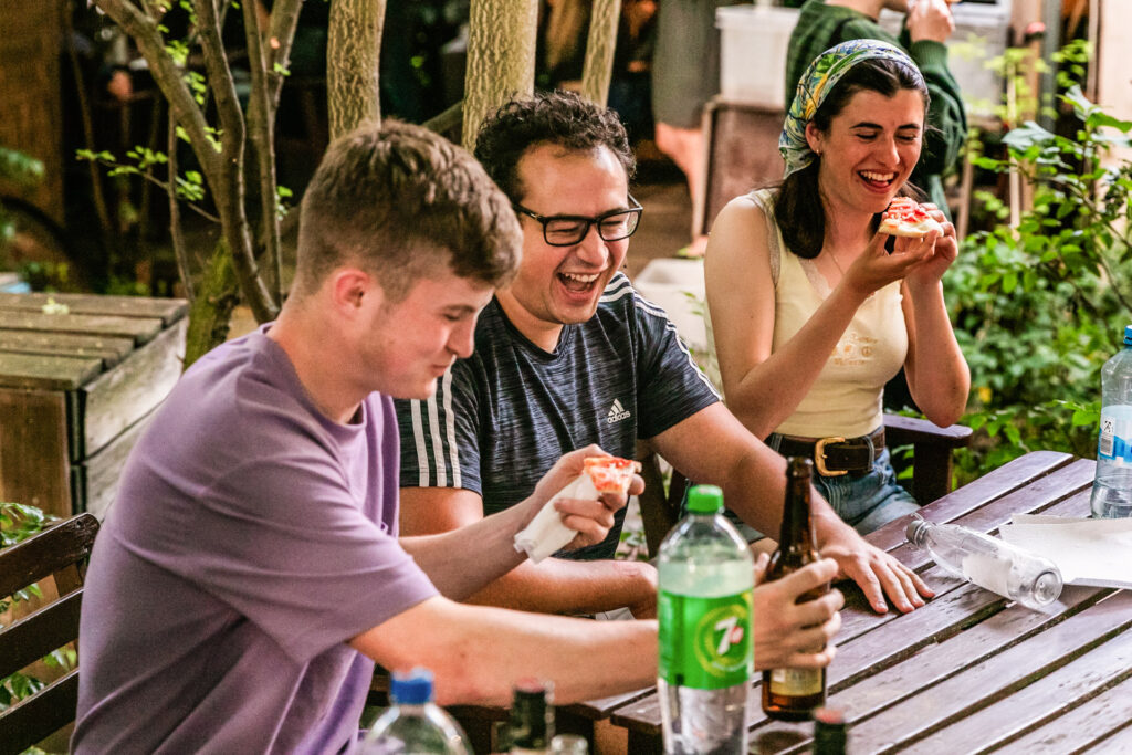 Junge Reisende genießen gemeinsam Pizza und Getränke im Außenbereich ihrer Unterkunft im EastSeven Hostel Berlin.
