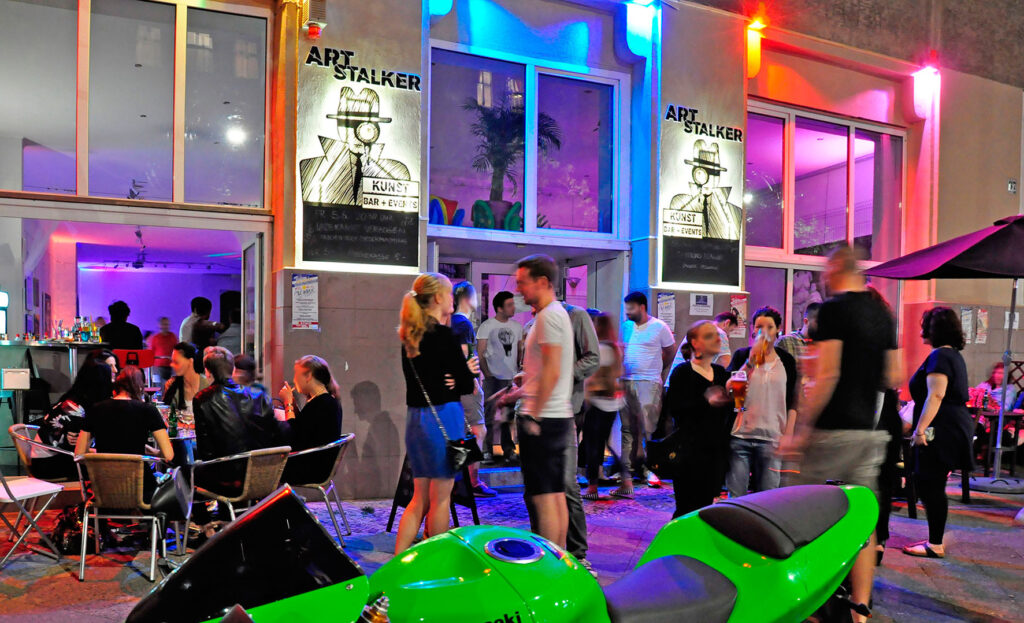 Belebte Bar „Art Stalker“ bei Nacht mit bunten Lichtern und vielen Gästen, ideal für außergewöhnliche Orte zum Geburtstag feiern in Berlin.