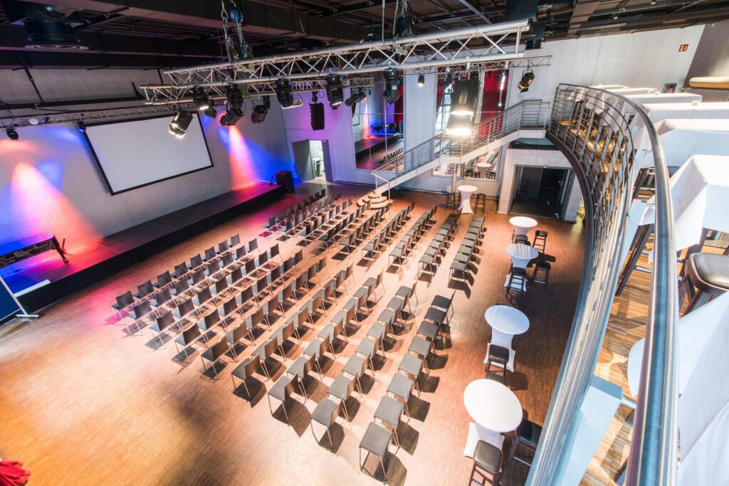 Moderne Veranstaltungshalle Palais in der Kulturbrauerei mit Bestuhlung, Bühne und Leinwand, perfekt für große Events und außergewöhnliche Orte zum Geburtstag feiern in Berlin.