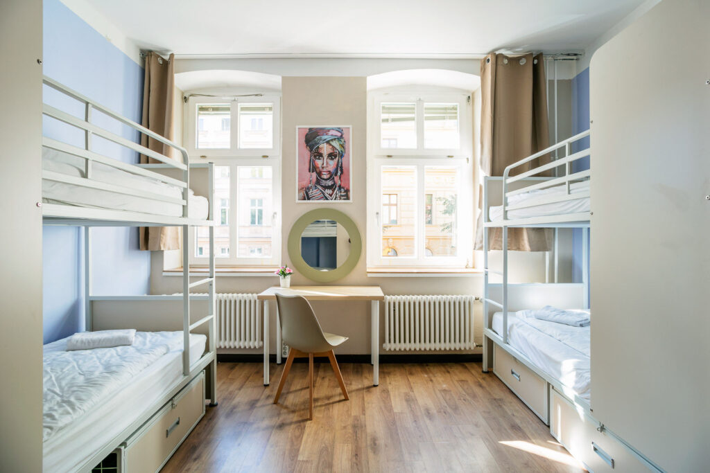 Innenansicht eines sauberen und freundlichen Hostel-Zimmers mit großen Fenstern in der Unterkunft EastSeven Berlin.