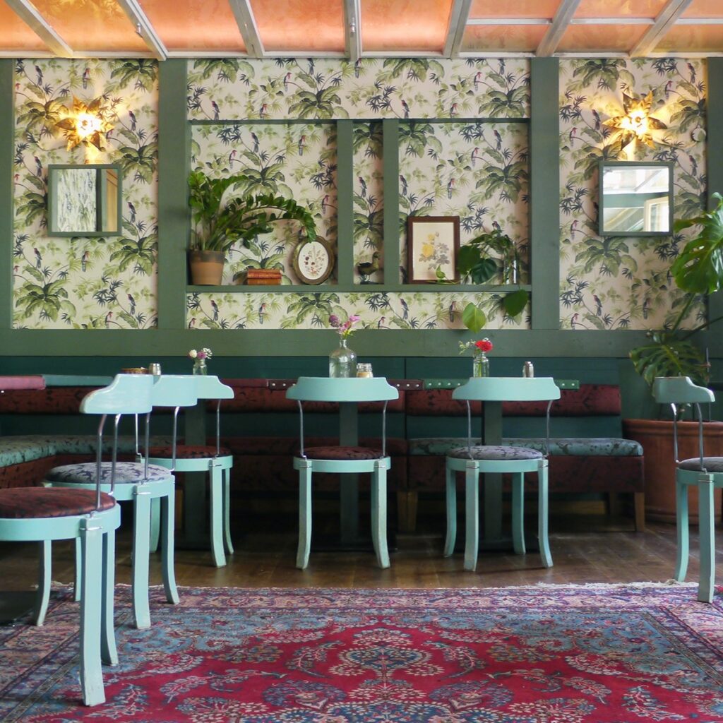 Verspielte Einrichtung mit floraler Tapete und Retro-Stühlen im House of Small Wonder, einem der verrückten Restaurants Berlin.